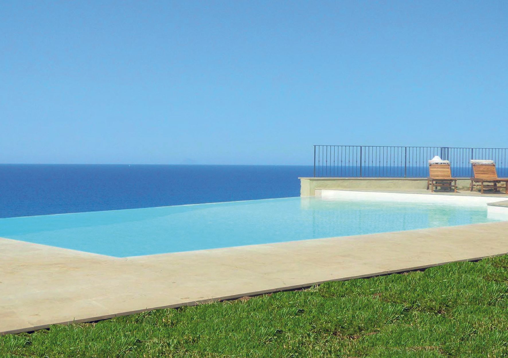 Piscina a sfioro con vista sull'oceano, con due sedie a sdraio; giornata soleggiata.