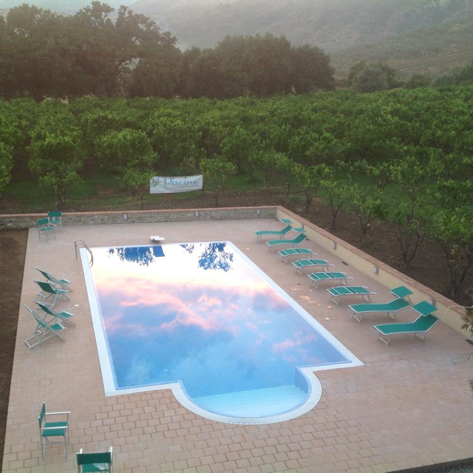 Piscina all'aperto con sedie a sdraio, alberi e riflessi del cielo.