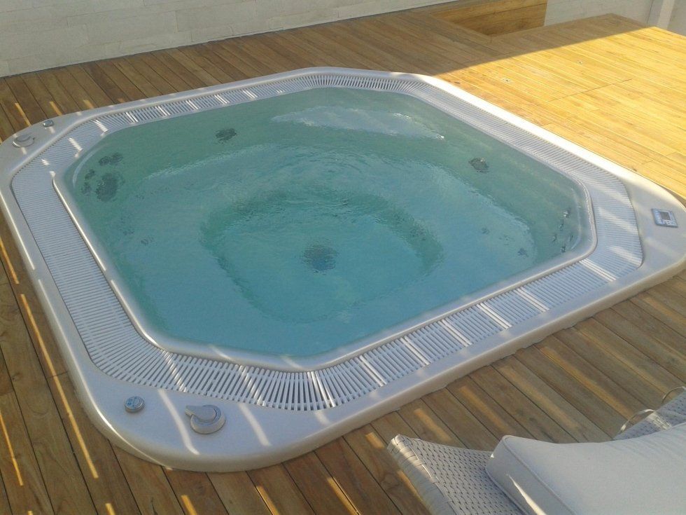 Vasca idromassaggio con acqua gorgogliante su una terrazza in legno esposta alla luce del sole.