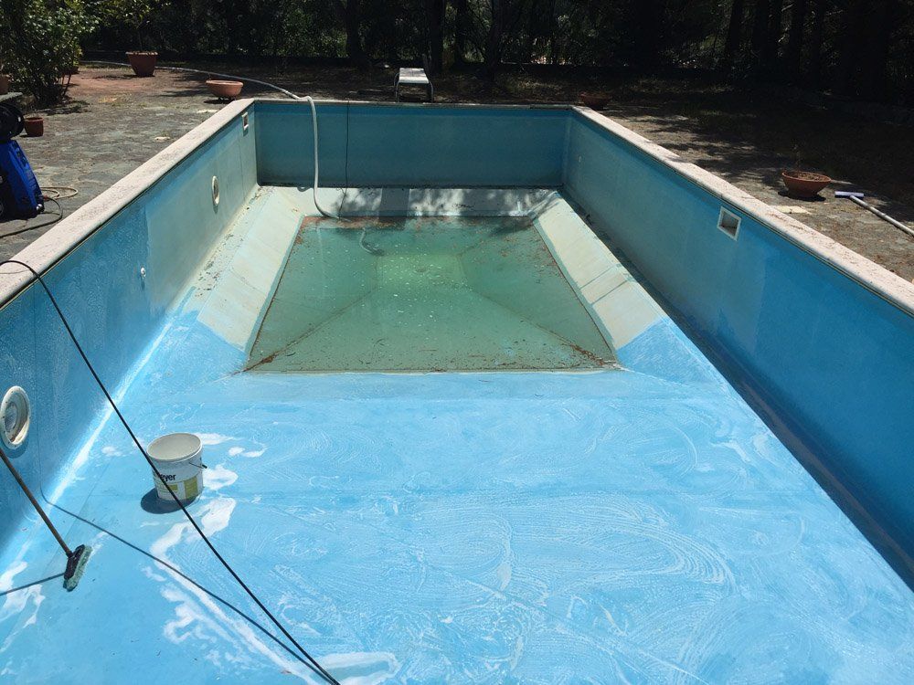 Piscina rettangolare vuota con interno azzurro, riempita con un po' d'acqua.