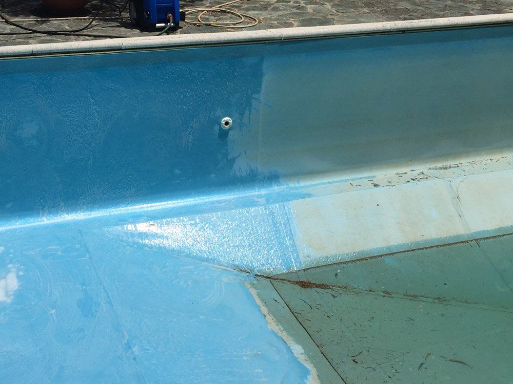 Vista parziale di una piscina con nuova vernice blu; in contrasto con una sezione più vecchia e sbiadita.