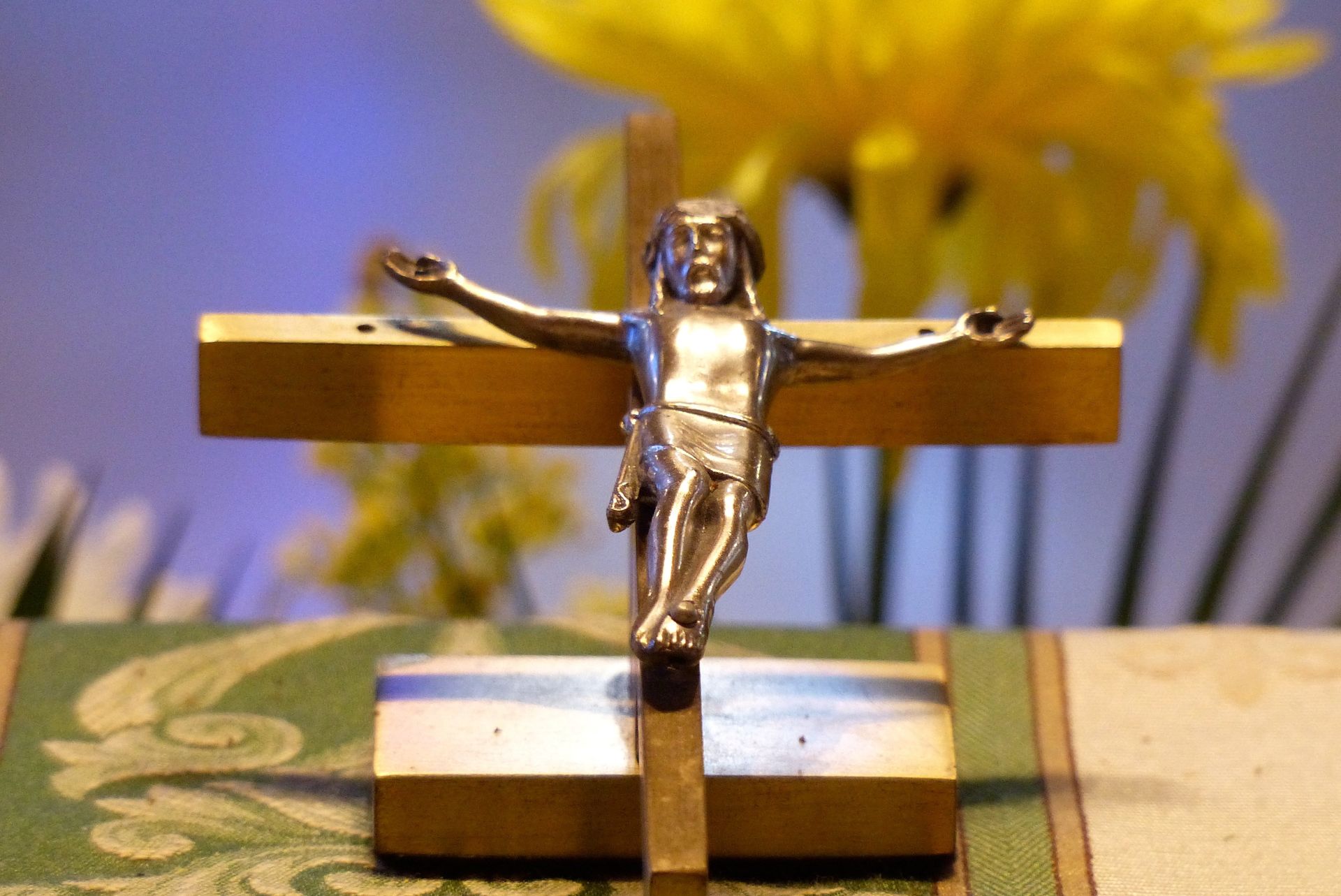 Crucifix: Silver Christ figure on a gold cross, yellow flower background.