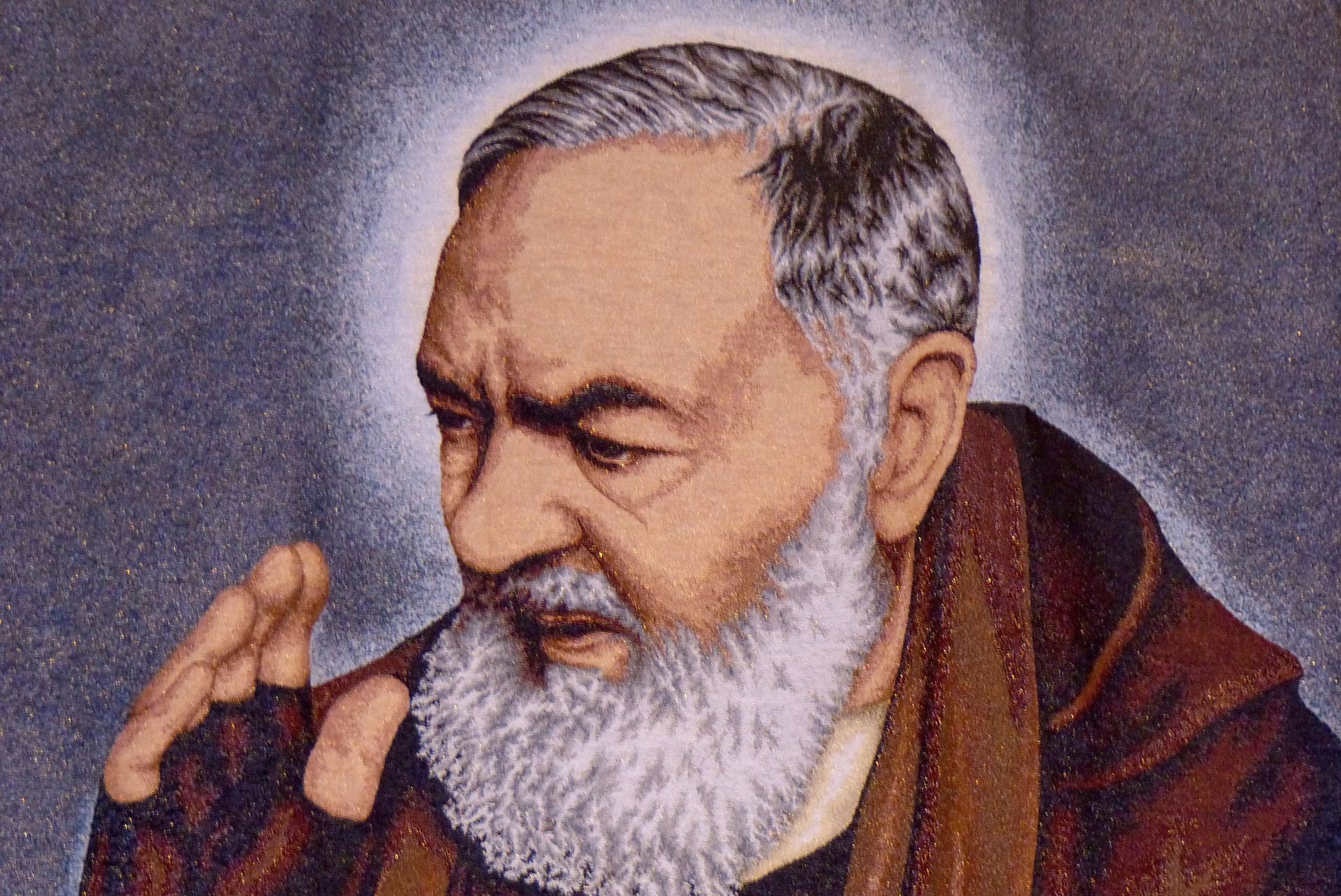 Portrait of Saint Pio of Pietrelcina with white beard and halo, praying.