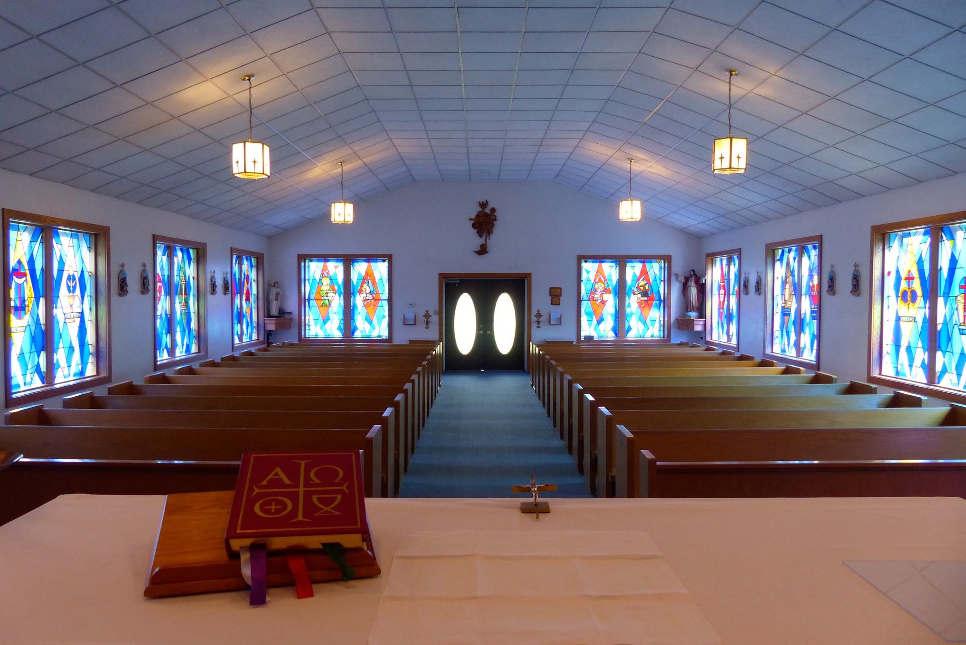 Interior view of a chapel with rows of wooden pews, stained glass windows, and a central altar.