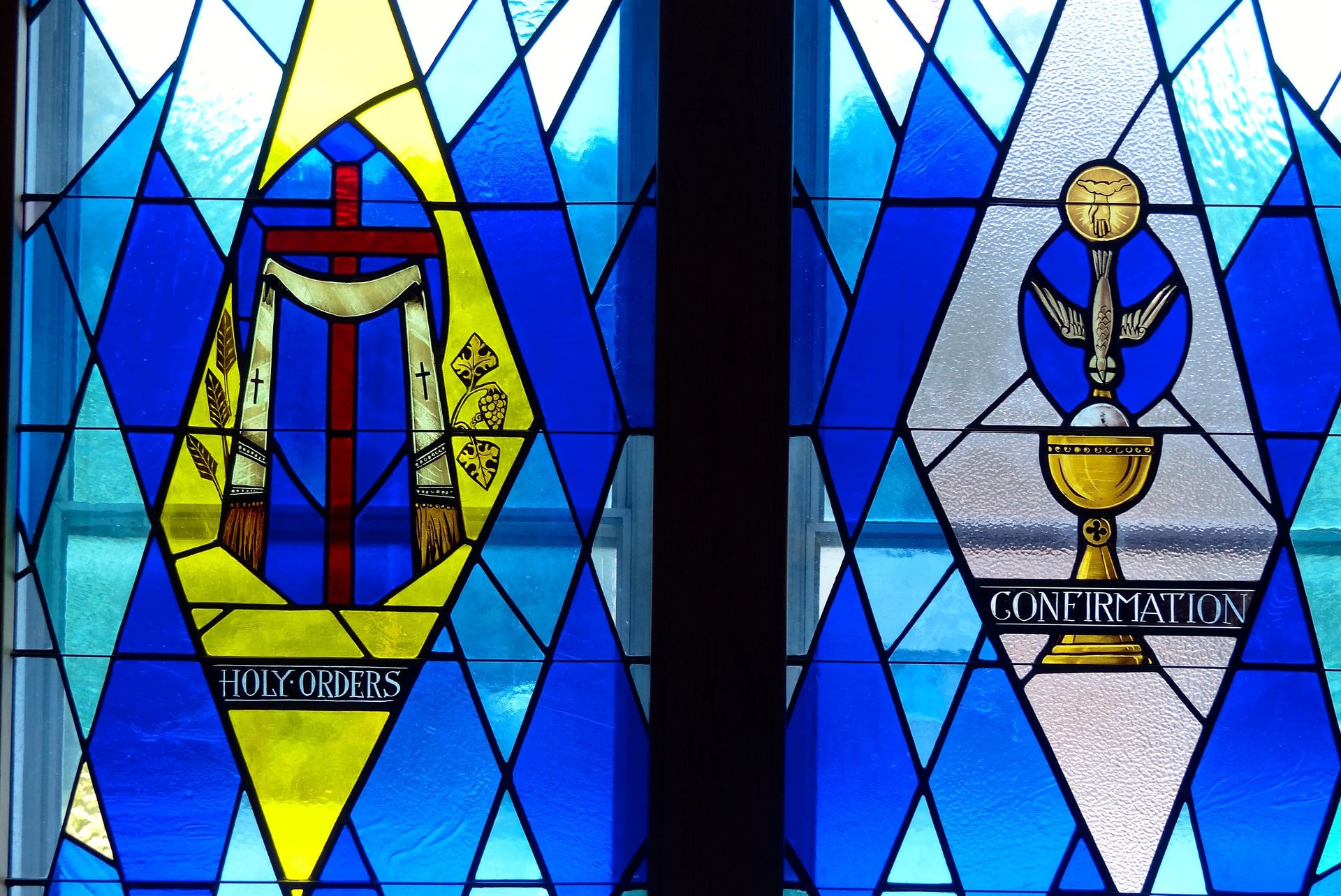 Stained glass windows: left, a cross and miter; right, a chalice and dove, surrounded by blue diamonds.