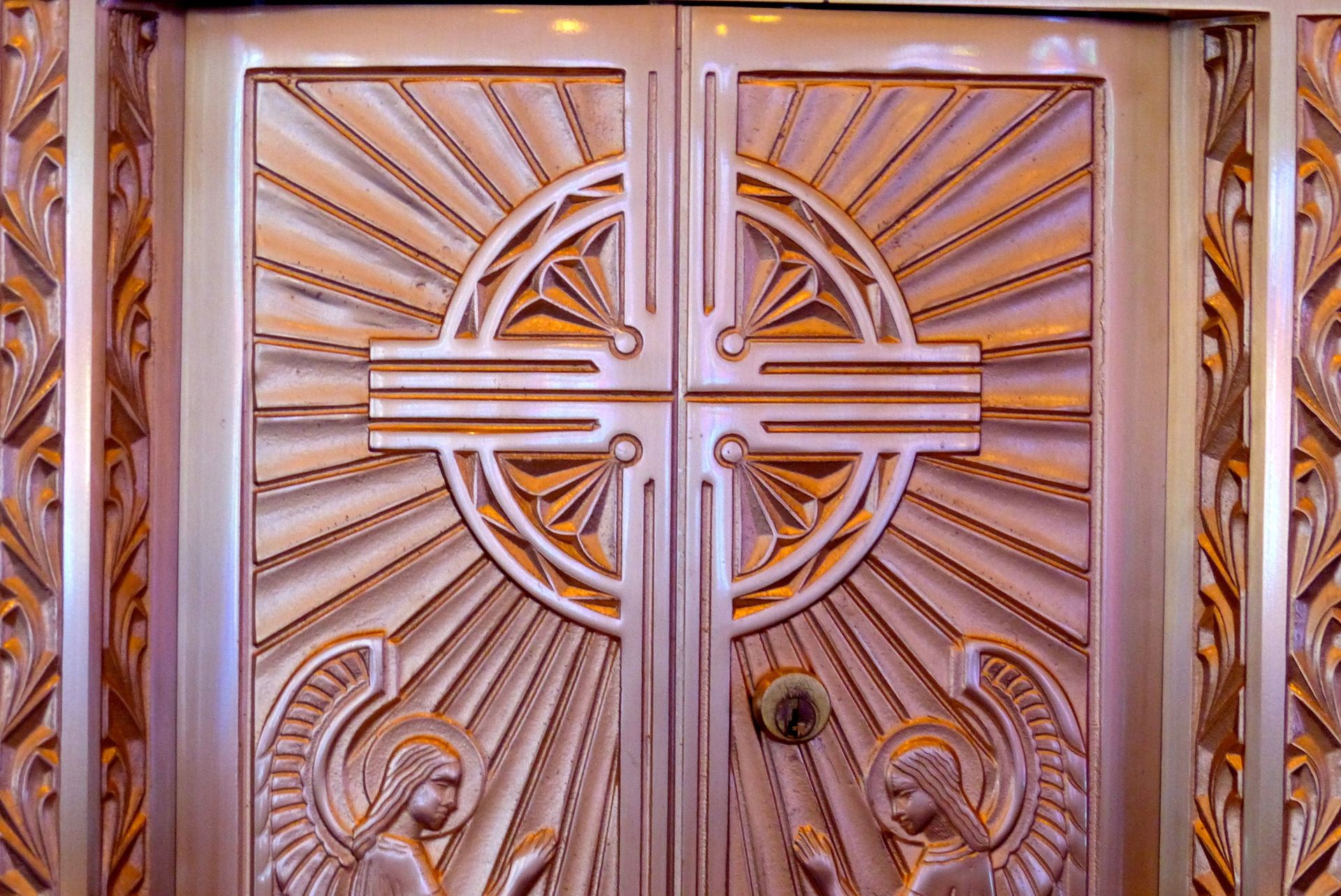 Ornate Art Deco double doors with sunburst and angel relief carvings.
