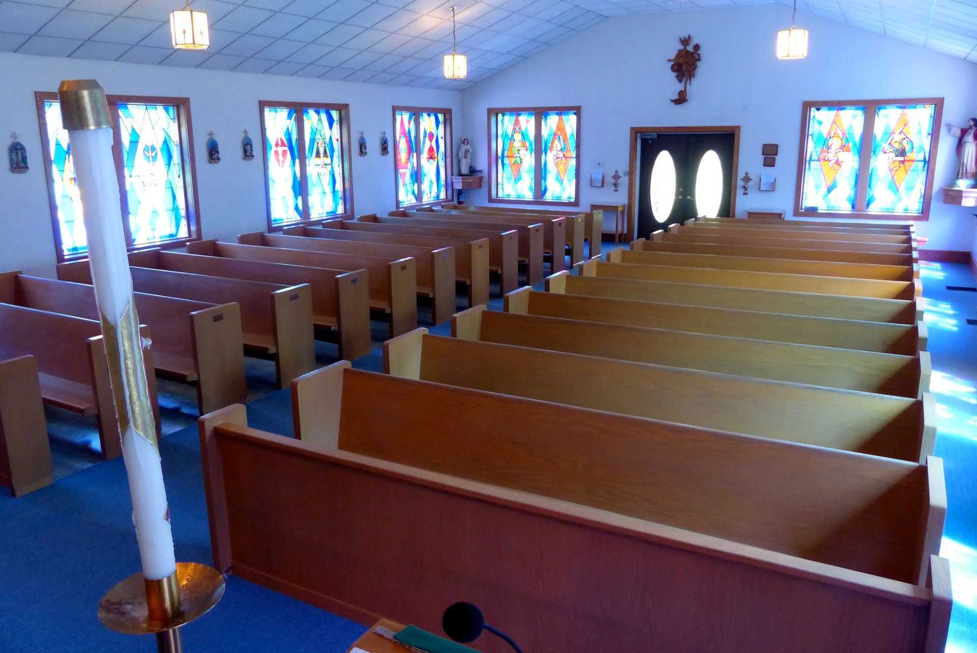 Interior of a church with wooden pews, stained glass windows, and a tall candle.