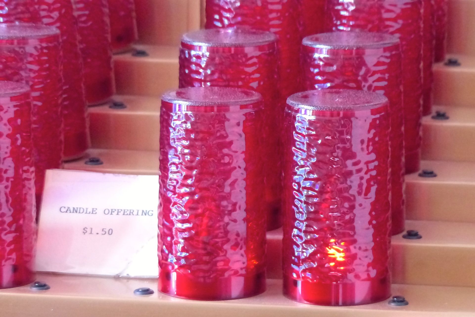 Red glass votive candles in a display for sale; sign reads 