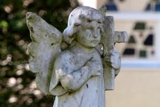Stone angel statue with wings, holding a cross, outdoors.