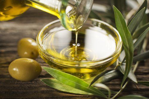 primo piano di una bottiglia mentre si versa olio di oliva vergine in una ciotola