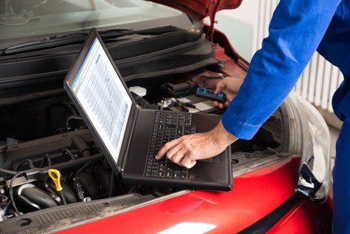 un computer portatile appoggiato sul motore d una macchina con il cofano aperto e il raccio di un meccanico mentre lo utilizza un computer portatile appoggiato sul motore d una macchina con il cofano aperto e il raccio di un meccanico mentre lo utilizza