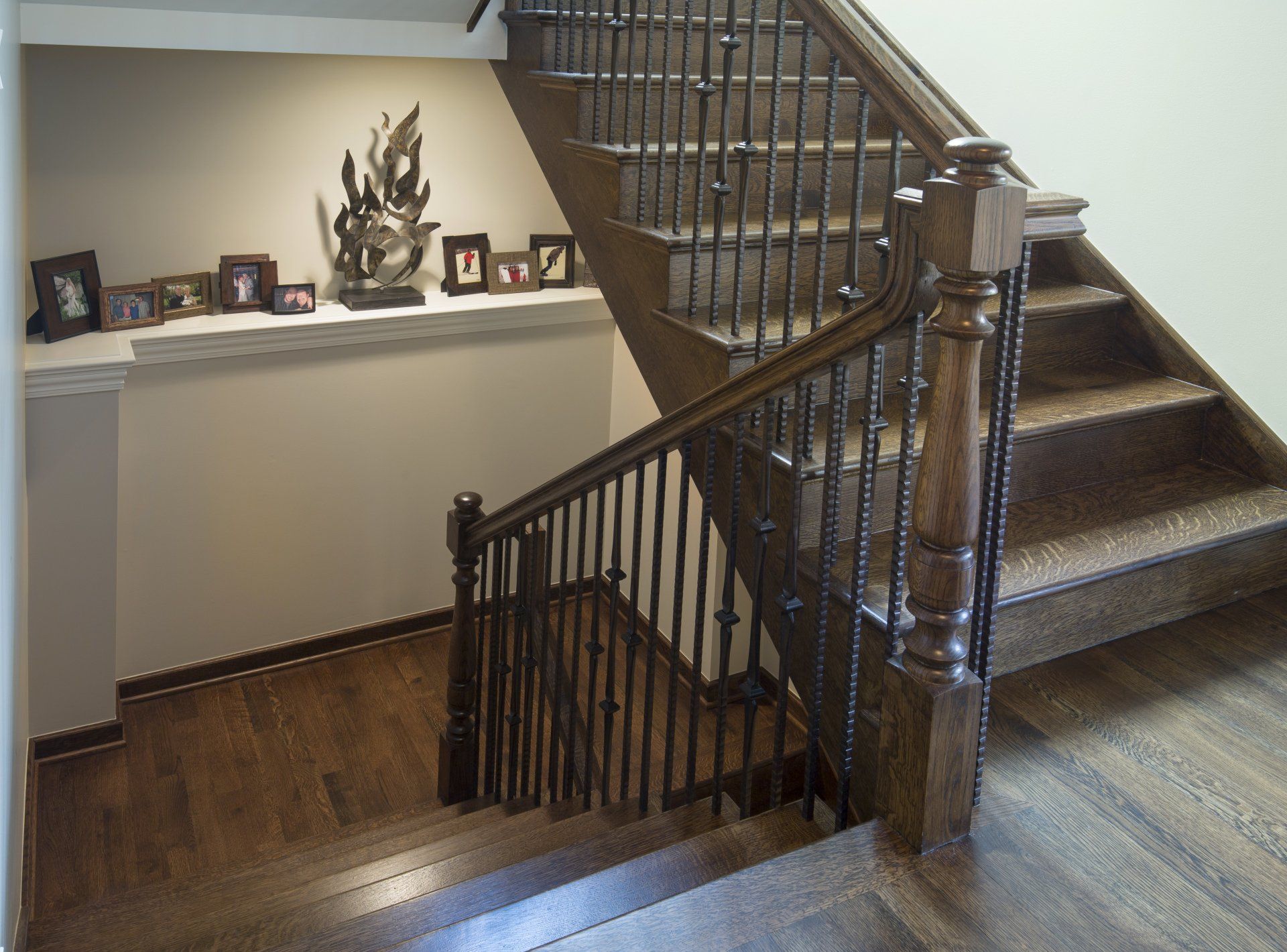 A wooden staircase with a metal railing and a shelf with pictures on it