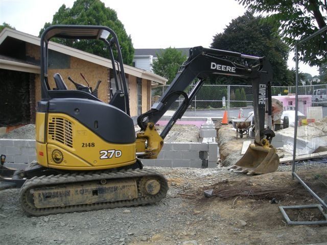 A yellow and black deere 270 excavator is parked in front of a house
