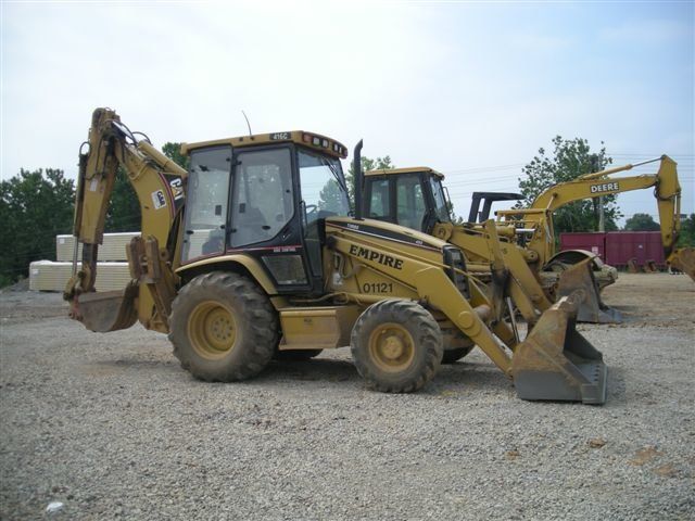 A yellow backhoe is parked in a gravel lot.