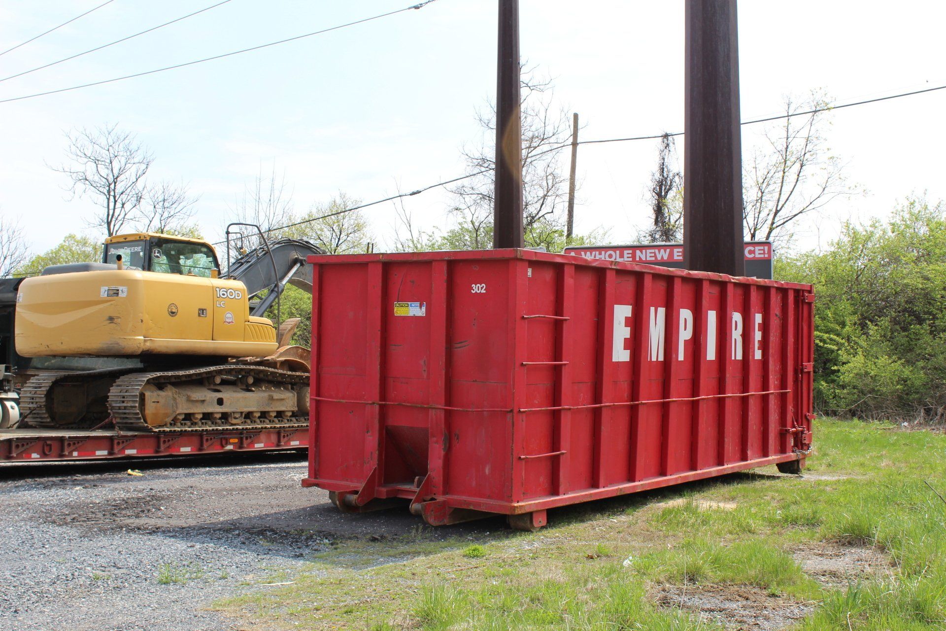 A red dumpster is sitting in a field next to a yellow excavator.
