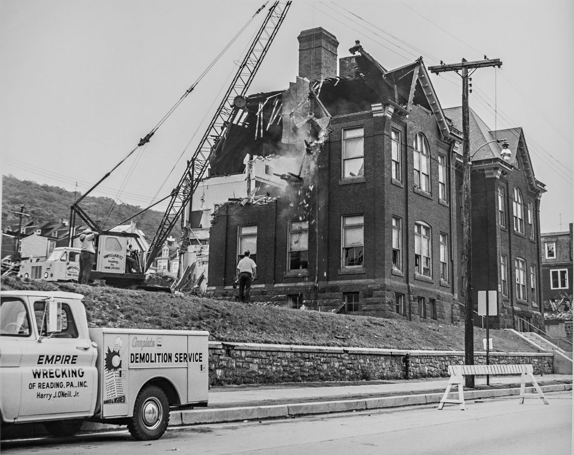 A demolition truck is parked in front of a brick building being demolished by Empire Wrecking.
