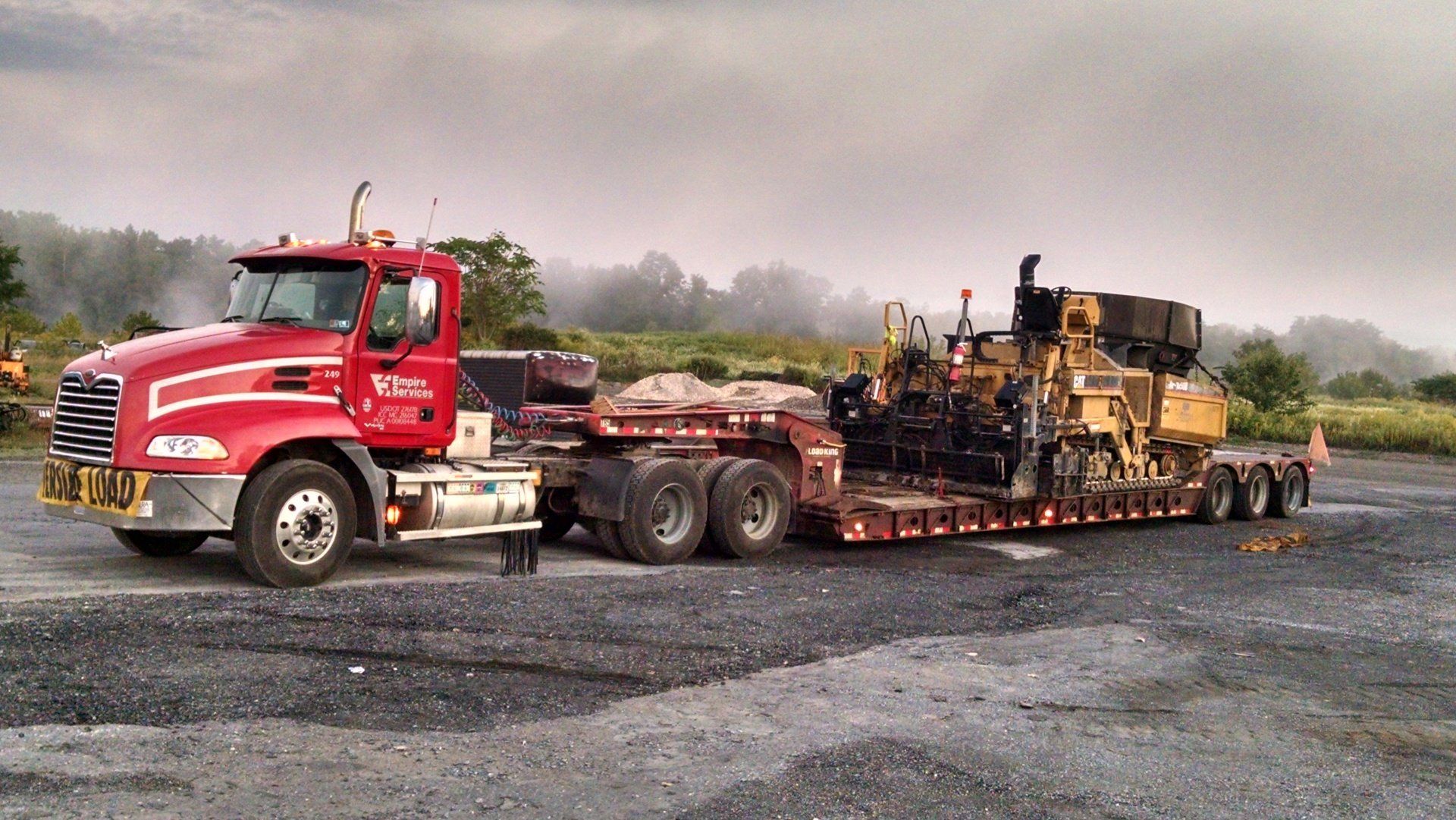 A red semi truck is carrying a bulldozer on a trailer