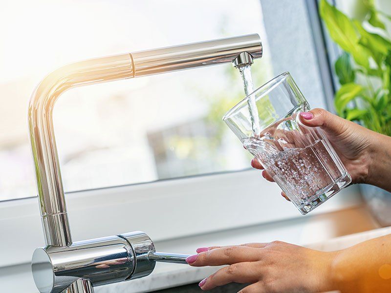 Person filling a glass with water from a chrome faucet in a bright kitchen.