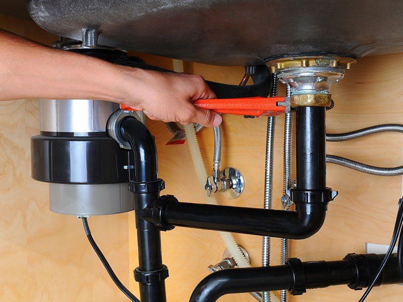 Person using a wrench on kitchen sink pipes under a wooden cabinet.