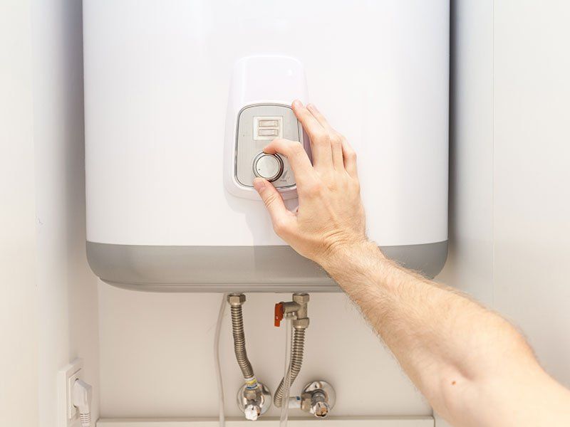 Hand turning the dial on a white water heater to adjust the temperature.