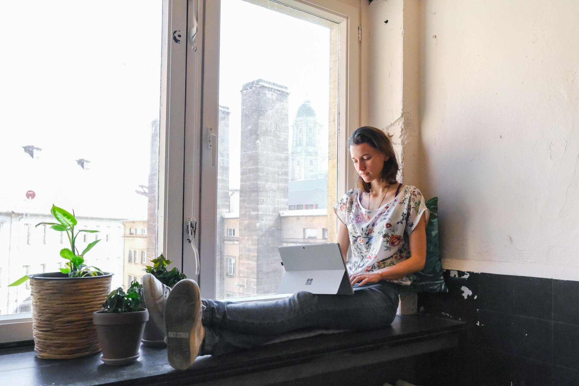 A woman on her laptop, by the window, thinking about her life situation
