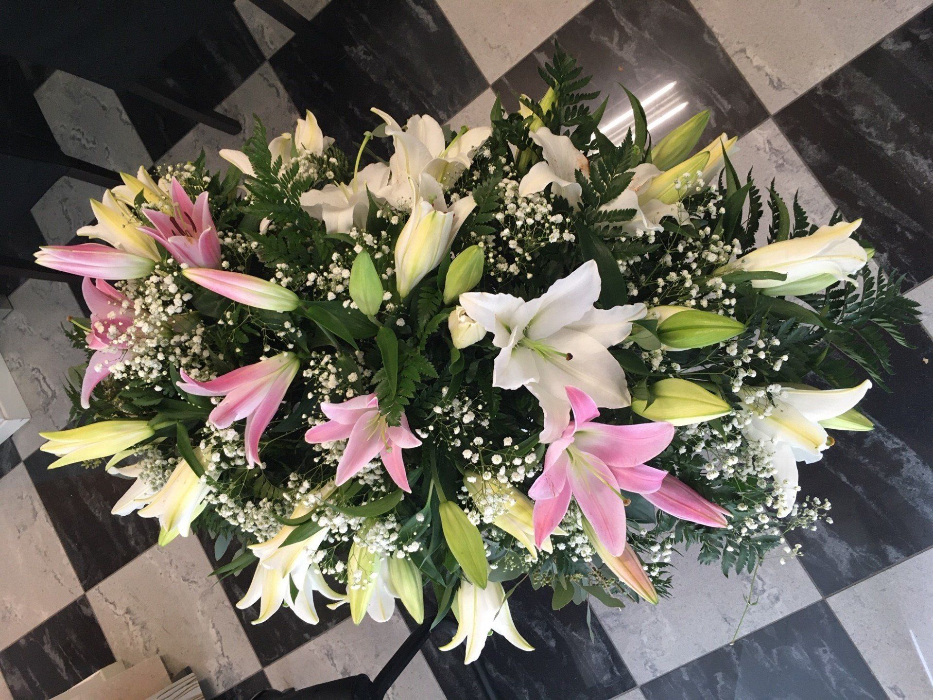 Composizione floreale con gigli bianchi, rosa e gialli, gypsophila e verde su pavimento a scacchi.