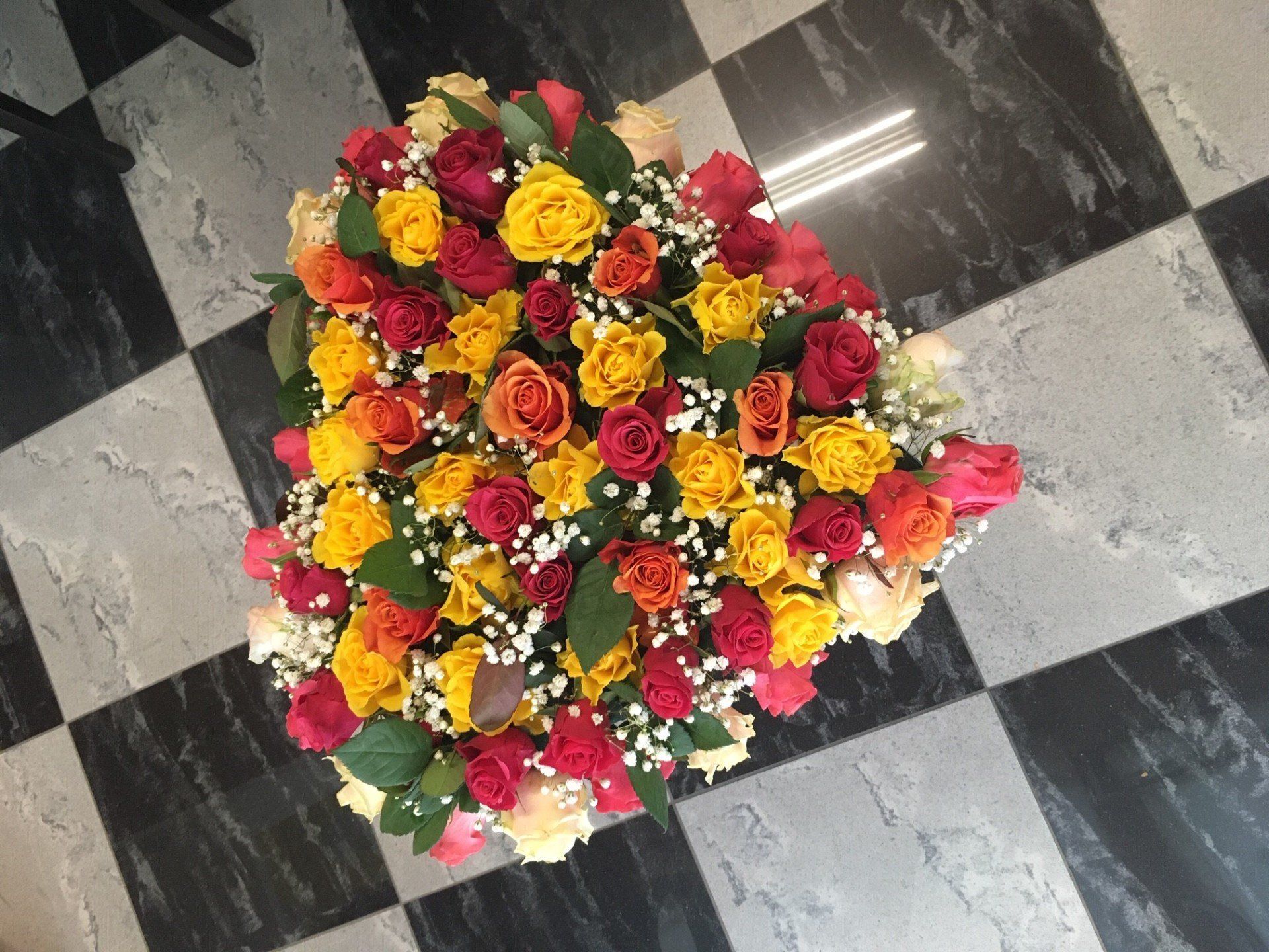 Composizione floreale a forma di cuore con rose rosse, arancioni e gialle e gypsophila su pavimento a scacchi.