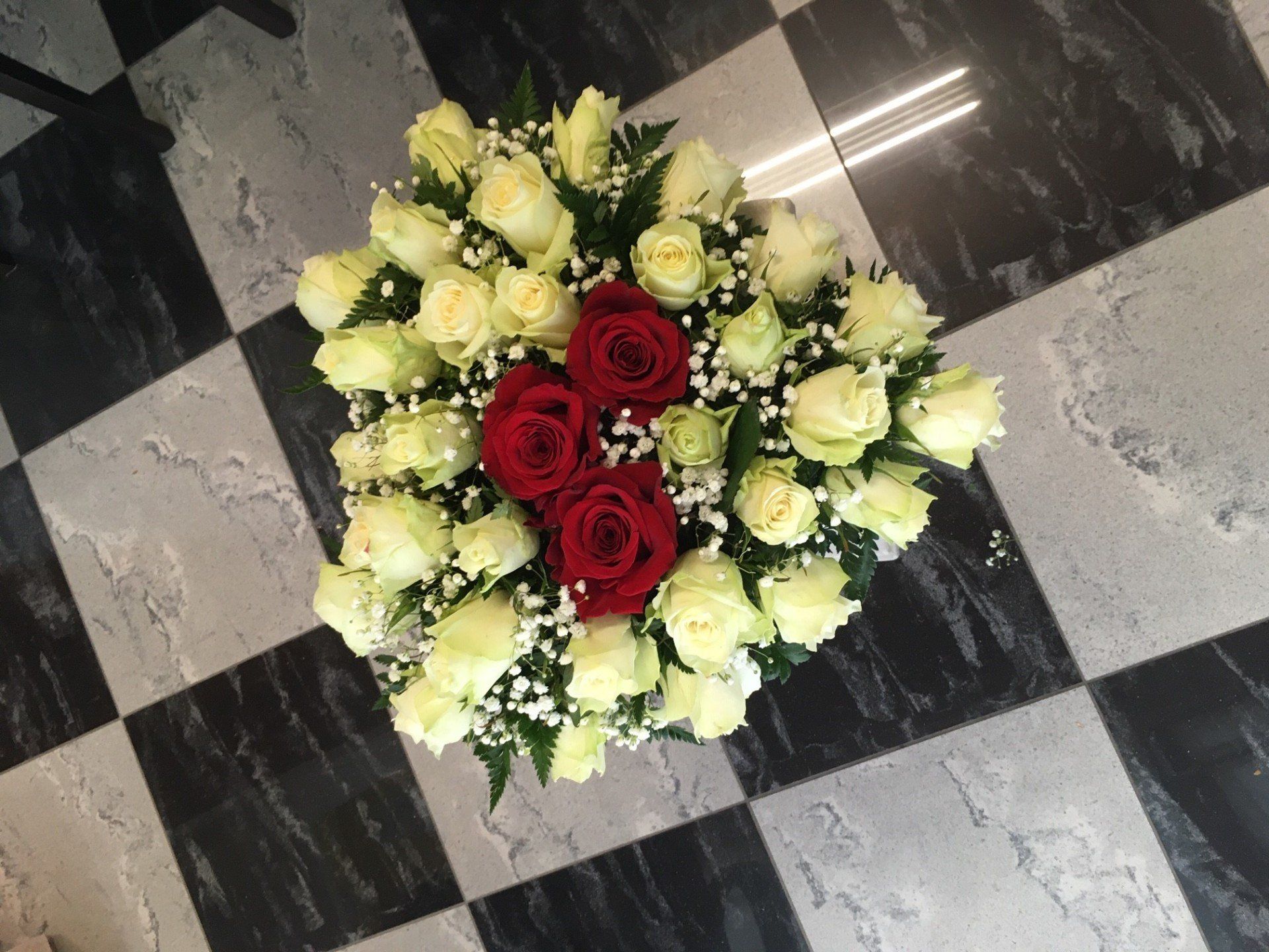 Composizione floreale rotonda con rose bianche e rosse su un pavimento piastrellato bianco e nero.
