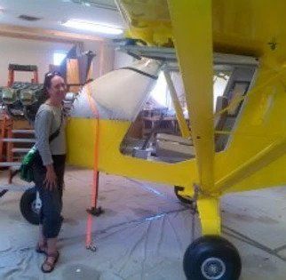 A woman is standing next to a yellow airplane in a garage.