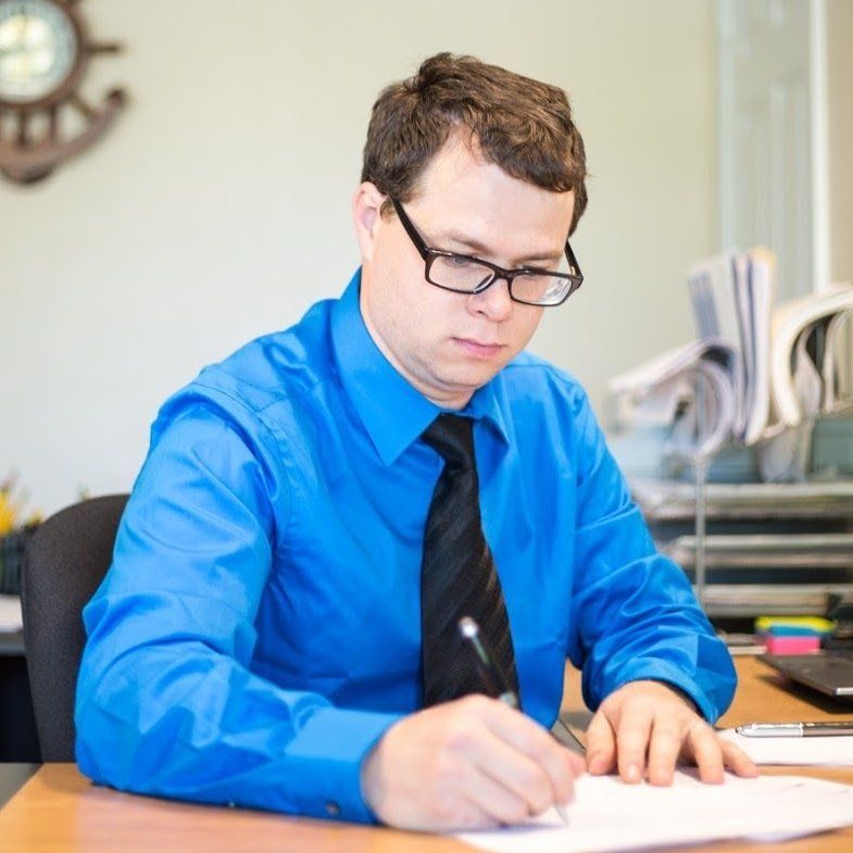 A man in a blue shirt and tie is writing on a piece of paper