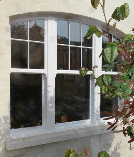White arched window with four panes on a stucco wall, partly framed by leafy branches