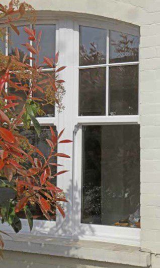 White-framed bay window in a stone wall, partly obscured by red-leafed foliage.
