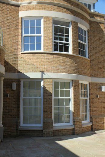 Brick building corner with curved upper windows and white-framed glass doors at ground level