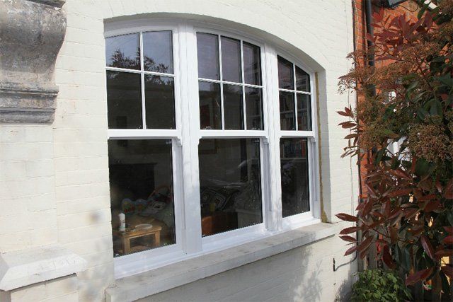 White arched window on a cream brick wall with reflections and a red-leaved plant beside it