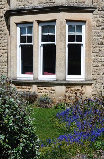 Stone house window with white trim, red curtains, and garden flowers below