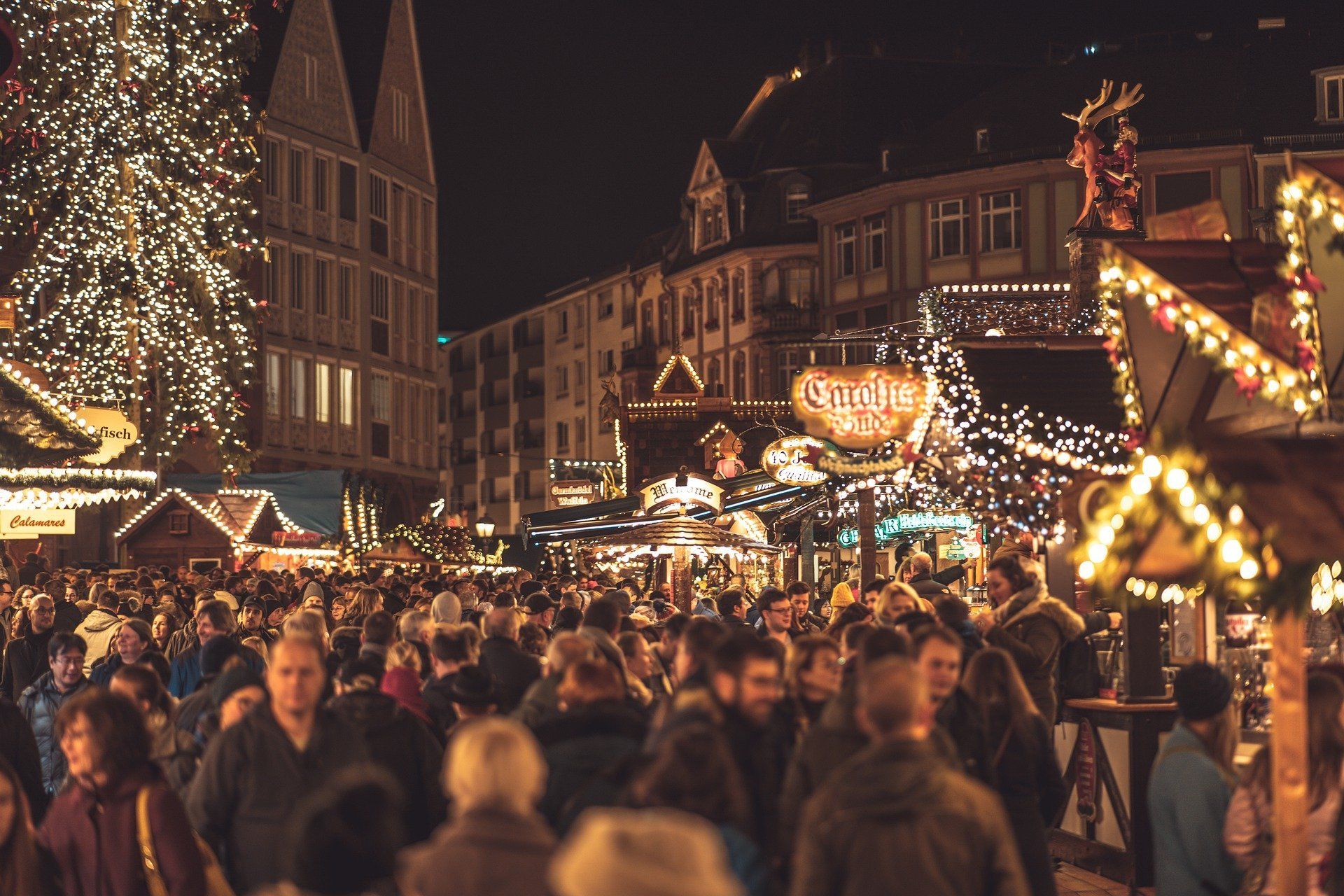 Eine Menschenmenge schlendert nachts über einen Weihnachtsmarkt.
