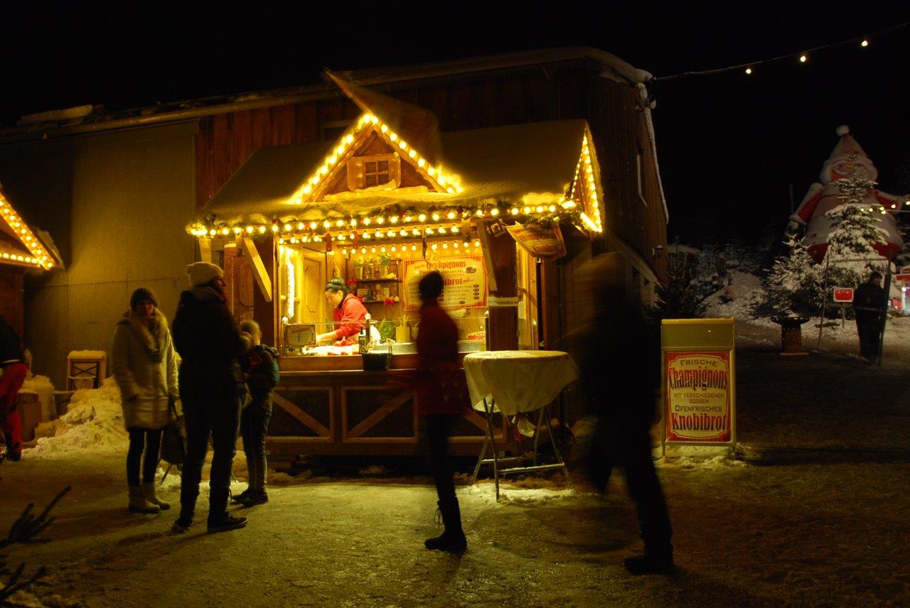 Eine Gruppe von Menschen steht nachts vor einem Weihnachtsmarkt.