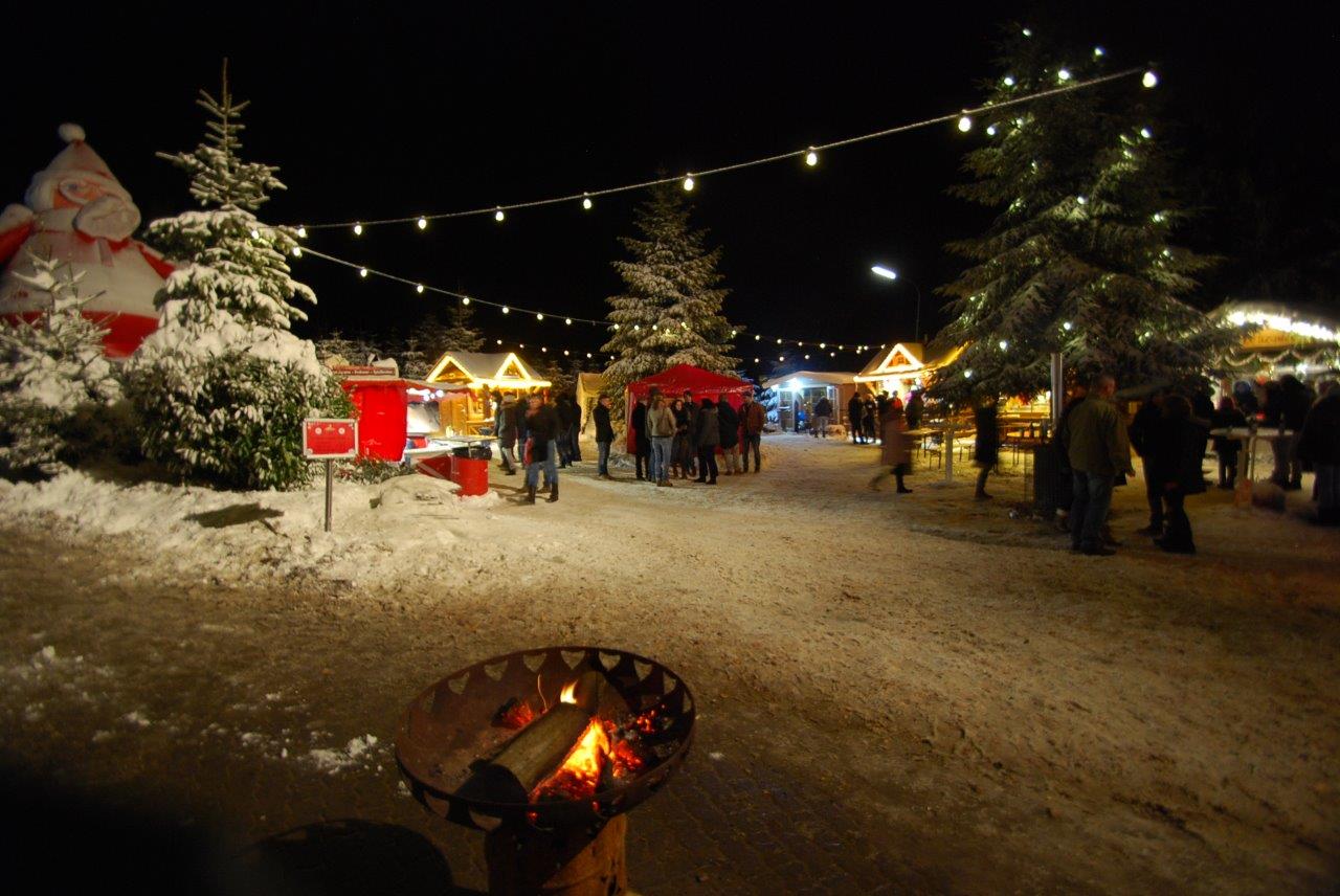 Eine Gruppe Menschen steht auf einem Weihnachtsmarkt im Schnee.