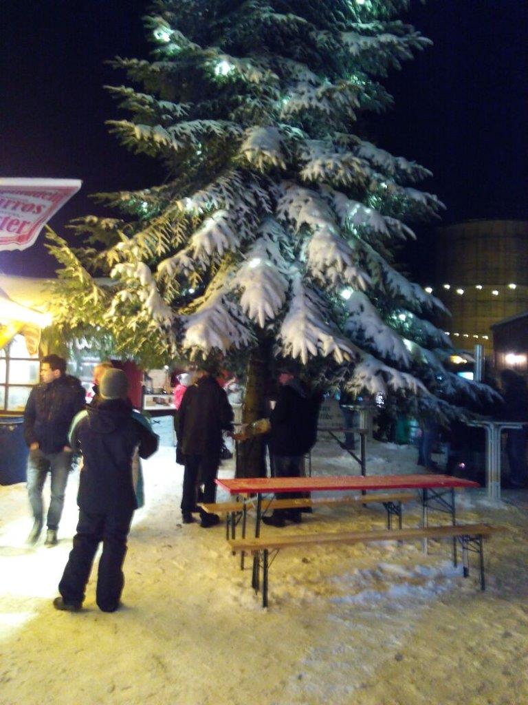 Eine Gruppe von Menschen steht um einen schneebedeckten Weihnachtsbaum