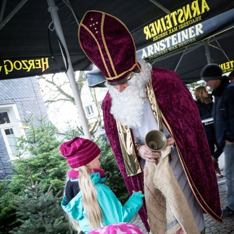 Ein Mann im Weihnachtsmannkostüm hält eine Glocke vor einem Schild mit der Aufschrift „Arnsteiner“