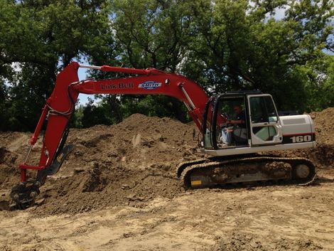 Red and white excavator digging dirt on a construction site.