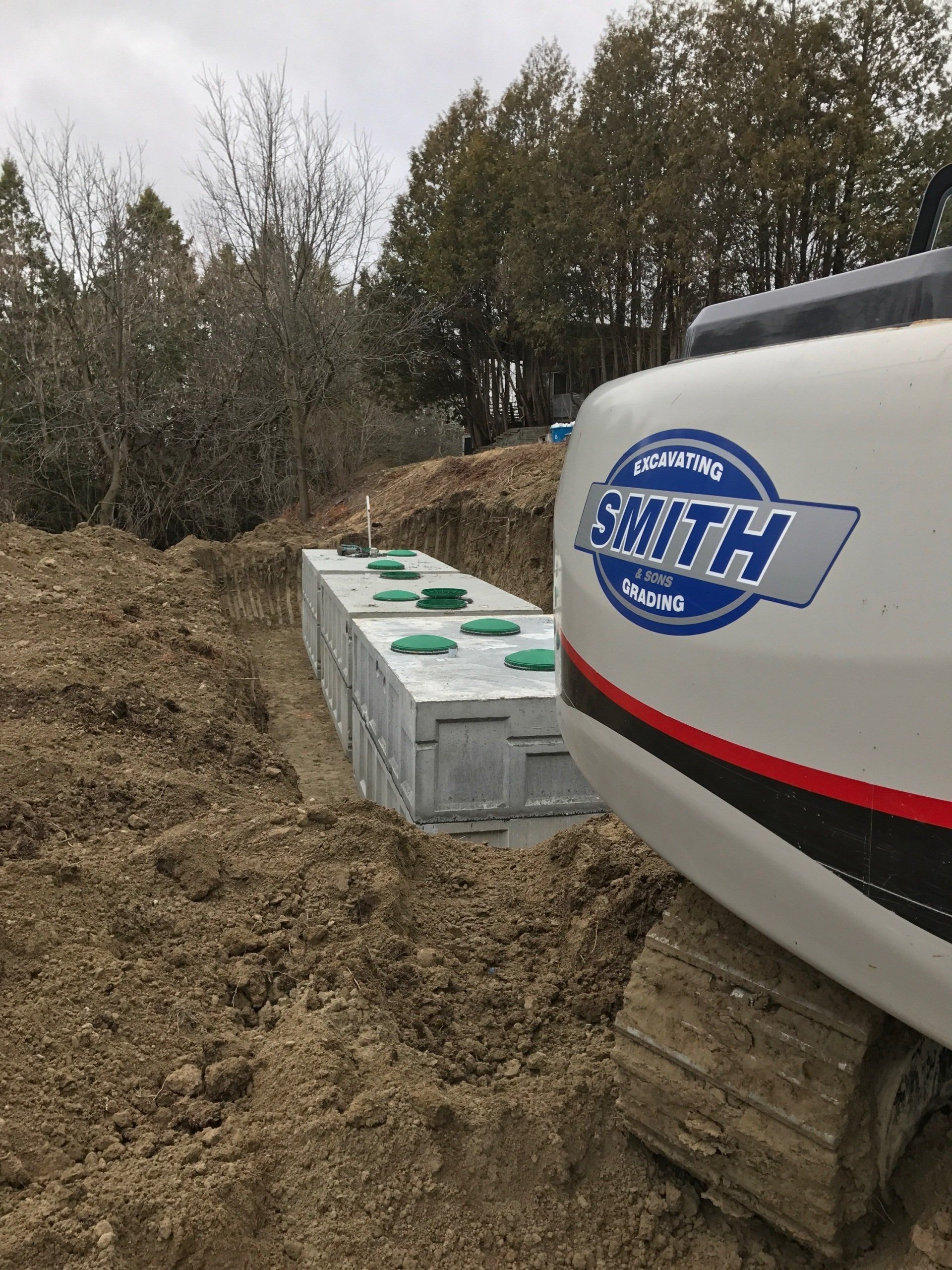 An excavator near a trench holding concrete septic tanks with green lids.