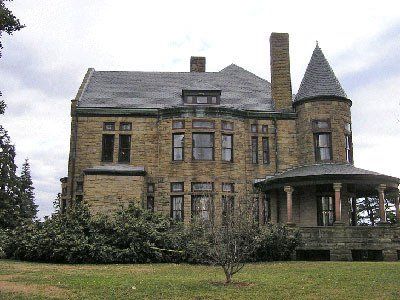 Stone mansion with a turret, porch, and chimney on a cloudy day.