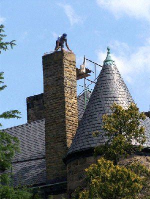 Man on chimney, blue cap, scaffolding, stone structure.