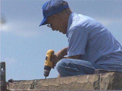 Man in blue shirt and cap uses a drill outdoors on a stone surface.