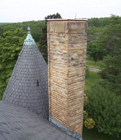 Stone chimney and slate-roofed turret against a backdrop of green trees.