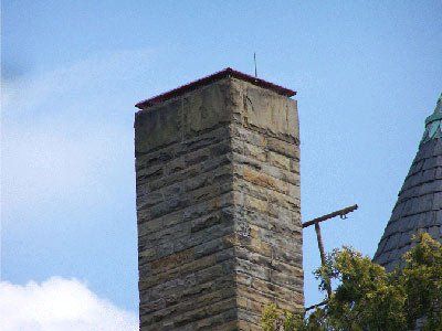 Stone chimney against a blue sky, topped with a red-brown surface and a small antenna.