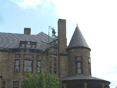 Man on scaffolding repairing chimney of a stone building with a turret.