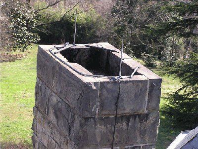 Stone chimney with metal wires and grassy background.