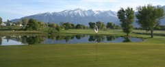 A golf course with a lake and mountains in the background.
